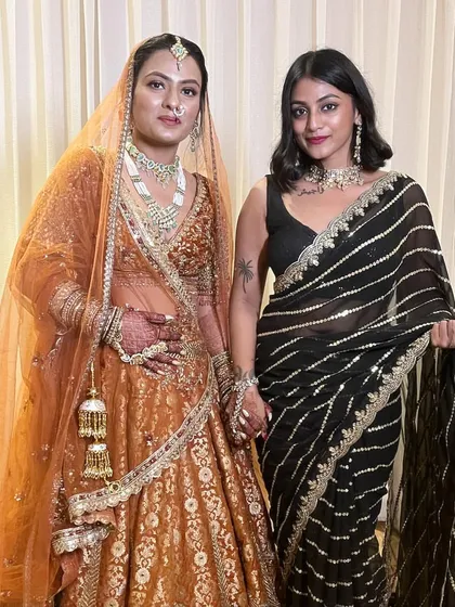 Standing with the beautiful bride. I'm wearing a black saree with striking silver and gold stripes, a modern take on traditional Indian wedding attire that is both elegant and eye-catching.