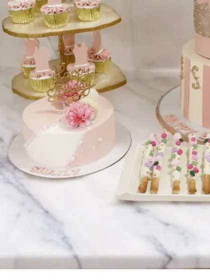Part of a beautiful ballerina-themed dessert table, this image shows the coordination between the main cake, themed cupcakes on a tiered stand, and delicate chocolate sticks. The consistent pink and gold palette creates a graceful and elegant look.