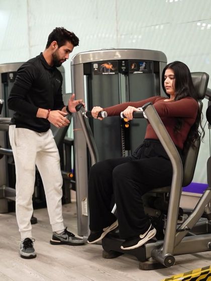 A trainer guides a member on the pec deck machine, ensuring she is using the correct range of motion to effectively target her chest muscles.