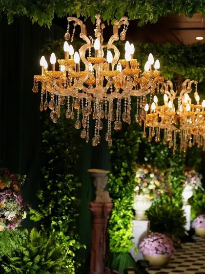 Ornate crystal chandeliers add a touch of opulence and create a warm, inviting glow, seen here in a lush, green-themed event space.