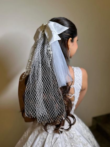A modern and chic half-updo featuring a white satin bow with a birdcage veil. This is a stylish and unique choice for a bachelorette party, civil ceremony, or reception.