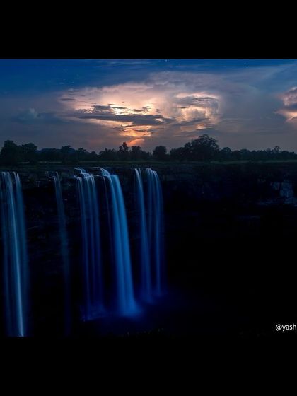 Another perspective of the waterfall at night, with the flowing water glowing blue under the moonlight and the dramatic clouds lit by a distant storm.