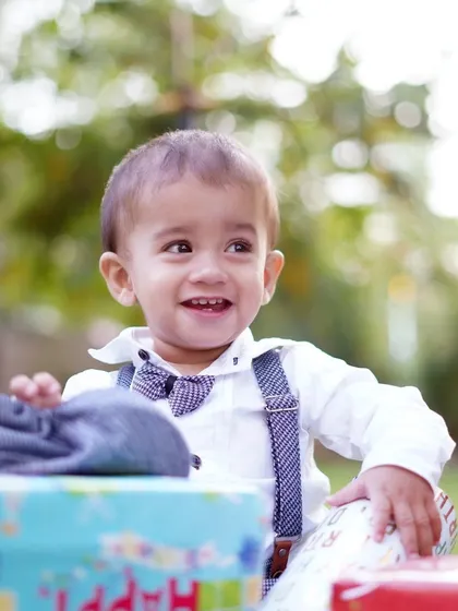 A bright, happy portrait of a toddler smiling, surrounded by birthday gifts during his outdoor park photoshoot.