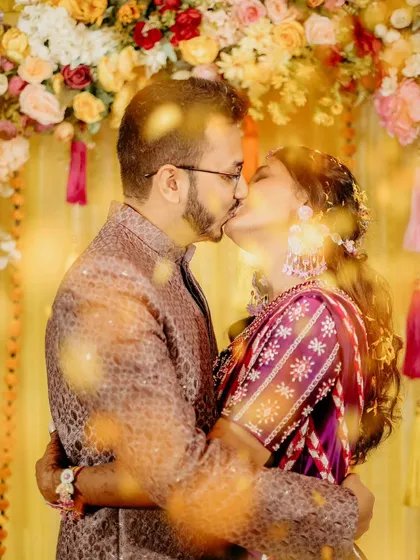 A close-up of the couple's kiss, with flower petals creating a beautiful, dreamy foreground. It's a romantic and artistic take on the haldi ceremony.