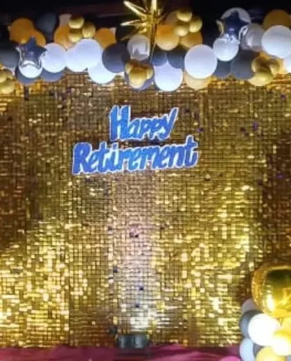 A stylish and fun retirement party decoration at a Gorai beach venue. We set up a shimmering gold sequin wall with a 'Happy Retirement' sign, framed by a black, gold, and white balloon arch for a perfect photo backdrop.