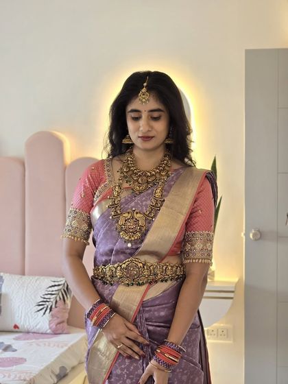 A full portrait of Laasya, showcasing the complete look with the pastel saree, heavy temple jewelry, and a contrasting pink blouse.