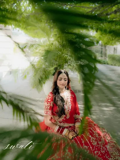 An artistic portrait of the bride seated amidst palm leaves, the play of light and shadow creating a painterly effect.