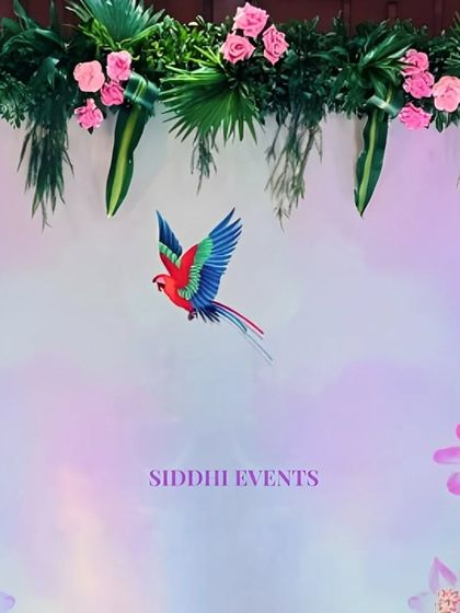 A close-up of a nature-inspired backdrop, featuring a printed parrot and flowers, topped with a fresh arrangement of pink roses and tropical leaves.