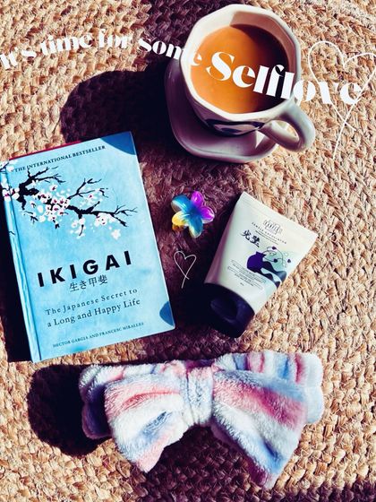 A 'self-love' flatlay with the book 'Ikigai', a cup of chai, and skincare items. This composition is ideal for brands in the wellness, beauty, and publishing spaces.