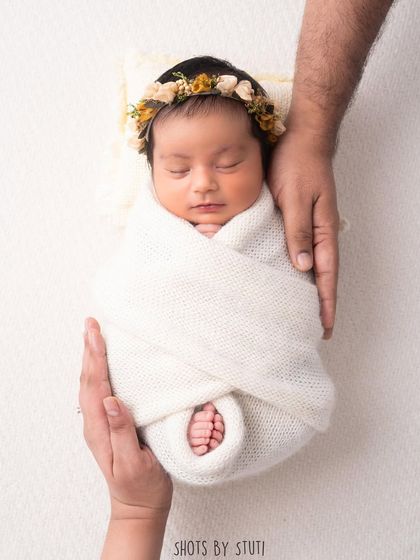 A swaddled newborn held securely in their parents' hands. This pose emphasizes the feeling of safety, love, and family connection.