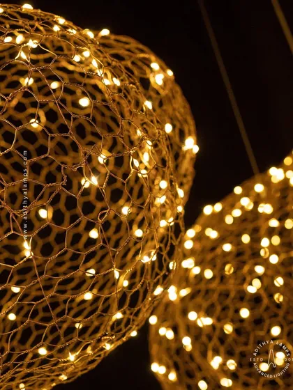 A detailed shot of the 'Clouds of Abundance' pendant light. You can see the intricate golden wire mesh and the hundreds of tiny LEDs that give the fixture its warm, sparkling glow.