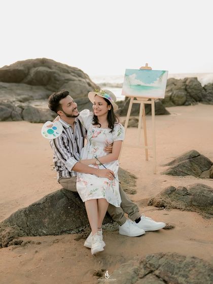 A romantic moment sitting together on a rock, with their painting nearby. This combines the theme with a classic, intimate couple portrait.