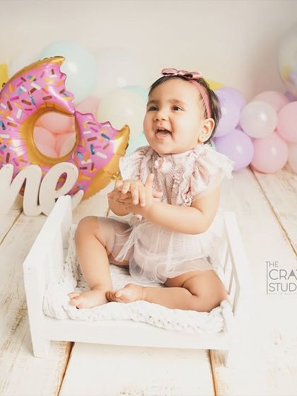 Clapping her hands with glee, this little one is having the best time at her donut-themed party, sitting on a tiny white bed.