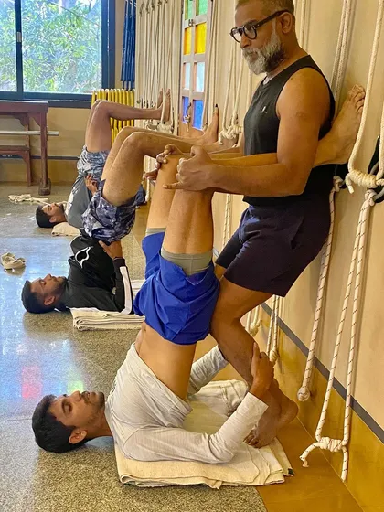 Here, a coach assists a tennis player in a supported shoulder stand variation using the wall. This pose is excellent for recovery, calming the nervous system, and improving circulation after intense training.