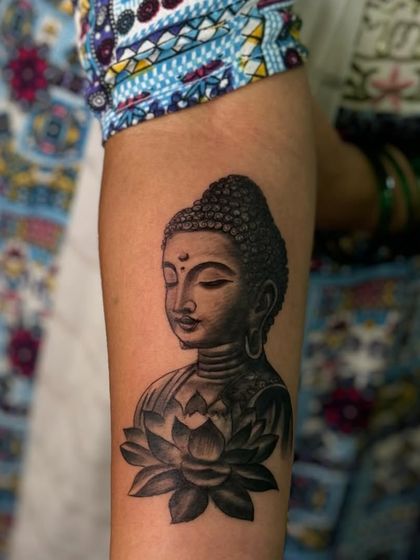A close-up shot of a beautifully shaded Buddha and lotus tattoo. You can see the fine details in the hair and the soft gradients on the petals.