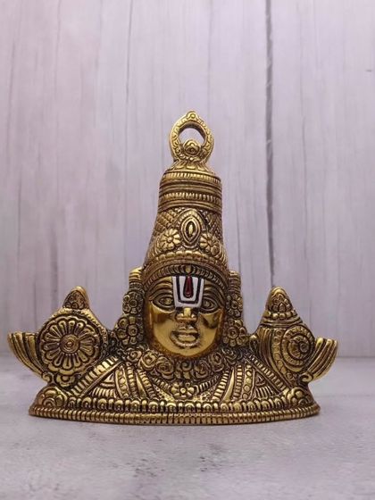 This Tirupati Balaji wall hanger in a rich gold finish is made of German silver and features detailed carvings of the Lord's face, shankha, and chakra.