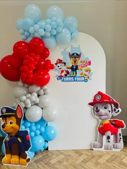 A classic Paw Patrol themed 4th birthday. The simple white backdrop is decorated with a red, white, and blue balloon garland and cutouts of Chase and Marshall.