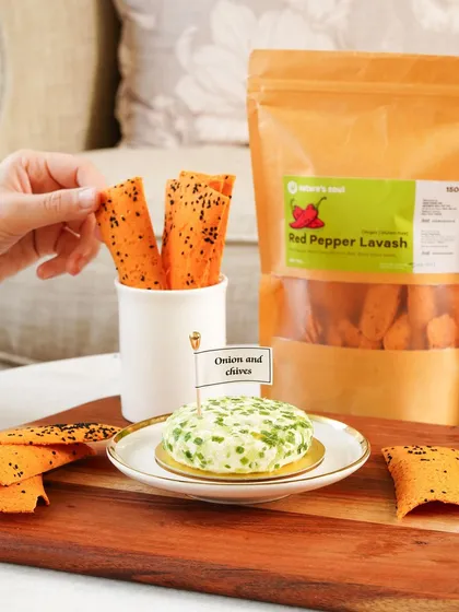 Red pepper lavash paired with an onion and chives cheese spread, styled on a wooden board for a rustic, gourmet feel.