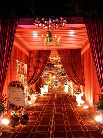 I design entrances that make a statement. This grand, red-draped walkway, illuminated by elegant chandeliers and lined with floral arrangements, created a dramatic and luxurious passage for guests, making them feel like royalty from the moment they arrived.