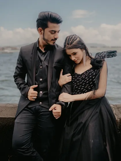 A tender moment of the bride resting her head on the groom's shoulder. Their coordinated black outfits and the sea background create a very chic and romantic image.