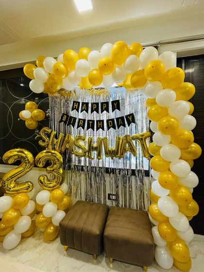 A 23rd birthday party with a gold and white balloon arch. This home setup includes a shimmer curtain and foil balloons for the name and age.
