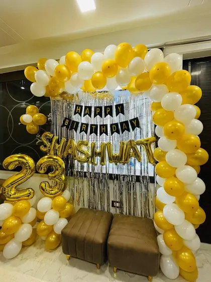 A 23rd birthday party with a gold and white balloon arch. This home setup includes a shimmer curtain and foil balloons for the name and age.