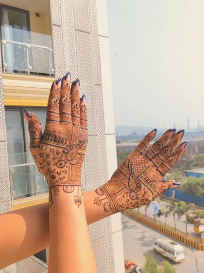This design prominently features parrots, a popular motif in bridal and festive henna. The way the hands are held up against the sky really shows off the detailed line work.