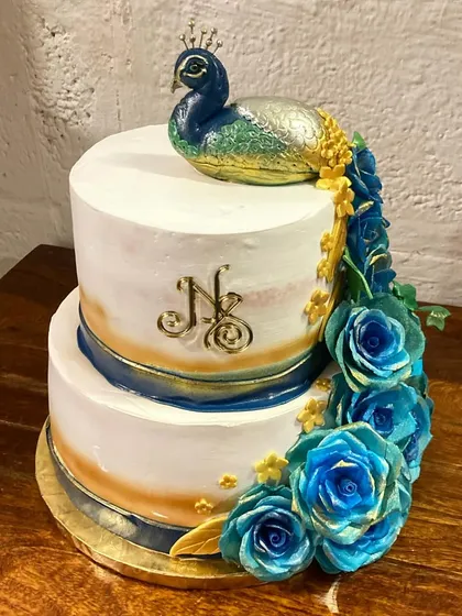I love bringing unique visions to life. This two-tier engagement cake features a majestic peacock theme, with a hand-sculpted peacock topper and a cascade of handmade blue sugar-paste flowers, all personalized with the couple's initials.