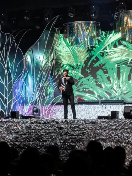 A solo performance on the grand Sangeet stage. The backdrop features a mix of abstract light structures and a vibrant tropical graphic on the LED screen, showcasing the versatility of our stage designs.