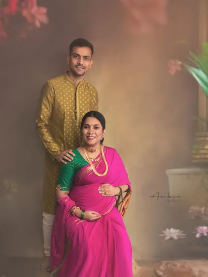A joyful couple portrait from a traditional maternity session. The vibrant pink saree and the partner's coordinated kurta create a visually harmonious and happy image.