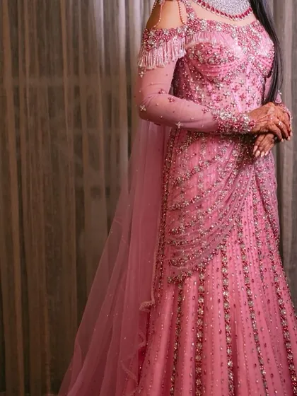 For the modern bride who dreams of a fairytale moment. This fully hand beaded pink gown features a flattering silhouette, cold shoulder details with delicate tassels, and a flowing train, designed for an unforgettable reception or gala.