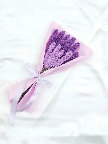 A simple and elegant bouquet of handmade crochet lavender. The shades of purple are wrapped in light pink paper and tied with a white ribbon, creating a soft and beautiful gift.