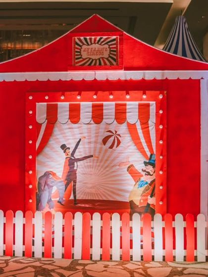 A charming photo booth designed to look like a classic circus stage. The illustrated backdrop and picket fence create a perfect spot for guests to capture memories of the day.