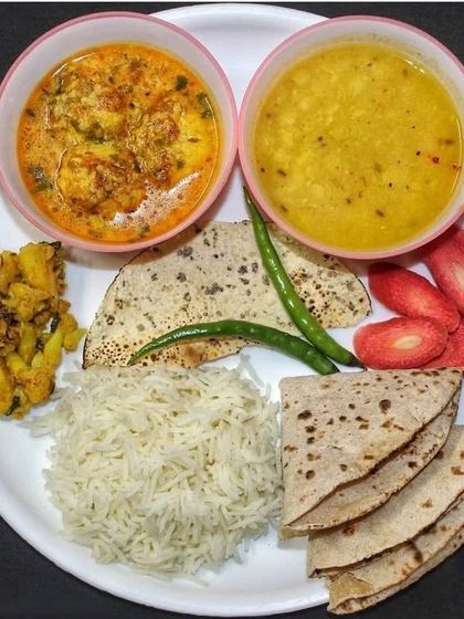 A plate full of love and flavor. This meal includes rice, rotis, dal, a creamy curry, a dry sabzi, and fresh carrots for a balanced and wholesome experience.