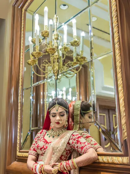 A classic bridal portrait, with the bride looking at her reflection in an ornate mirror, a grand chandelier adding to the luxurious feel.