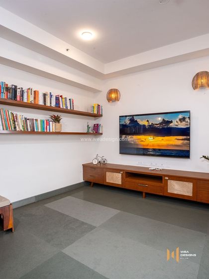 The family room or den in the earthy-themed apartment, with simple wooden bookshelves and a media unit that complements the natural aesthetic.