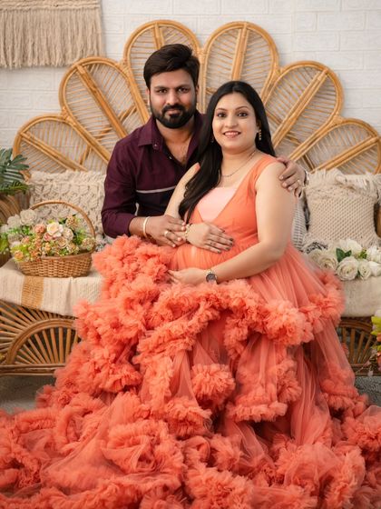 A warm and loving portrait of the couple seated together on our boho set. The rich peach color of the gown and the earthy tones of the decor create a cozy and inviting atmosphere for this pregnancy photoshoot.
