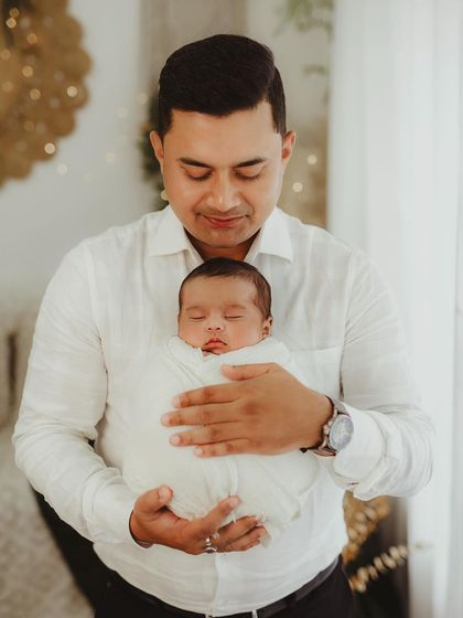 A father gazes lovingly at his swaddled newborn. The soft, warm tones of the photo enhance the feeling of tenderness.