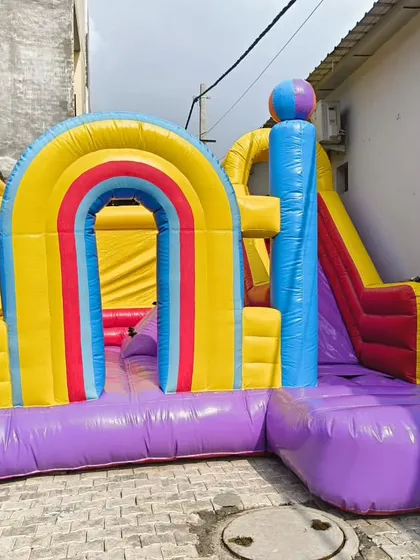 A vibrant bouncy with rainbow arches and a side slide. The bright color palette makes it highly visible and attractive for kids.
