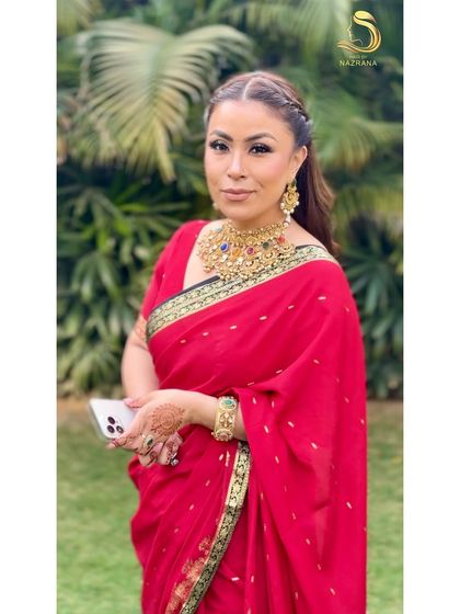 A beautiful client wearing a red saree with her hair in a half-up braided crown style.
