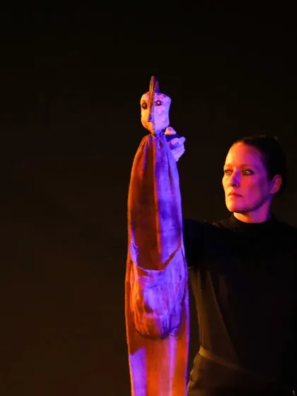 A puppeteer from the French show 'Wings & Roots' holds a uniquely crafted wooden puppet. The performance uses evocative, abstract puppets to adapt Stefan Zweig's 'The Legend of the Third Dove'.