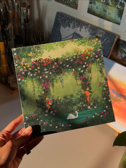 Holding up the finished swan lake painting. This piece was made with acrylics on a square canvas and is a perfect example of the dreamy, cottagecore style you can commission.