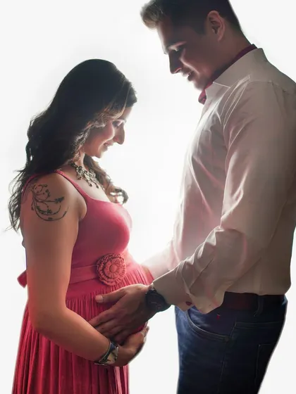 A beautifully backlit silhouette of a couple sharing a quiet moment. This high-contrast image focuses on their profiles and the gentle touch on the baby bump.
