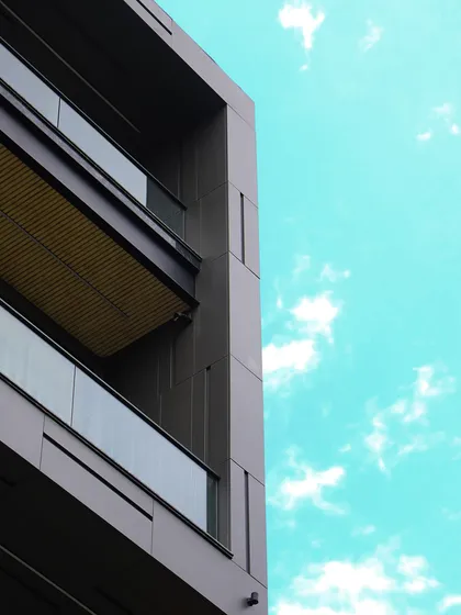 An upward-looking shot of the facade against the sky, highlighting the clean, modern lines of the grooved panels and glass balconies. The design creates a powerful geometric statement.