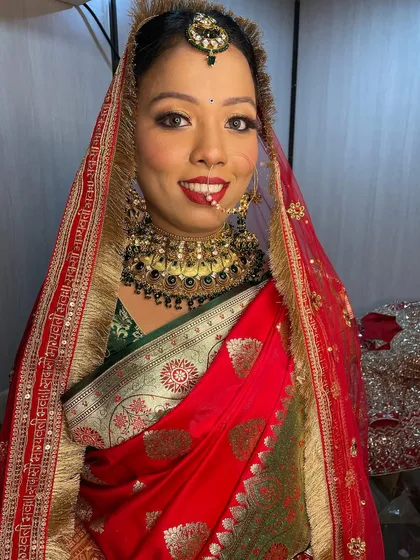 A smiling portrait of the bride in her traditional red Banarasi saree and heavy gold jewelry.