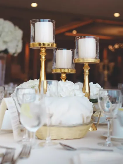 A classic and elegant table setting with white florals and golden candle holders. This timeless look is perfect for a sophisticated wedding reception or formal dinner.