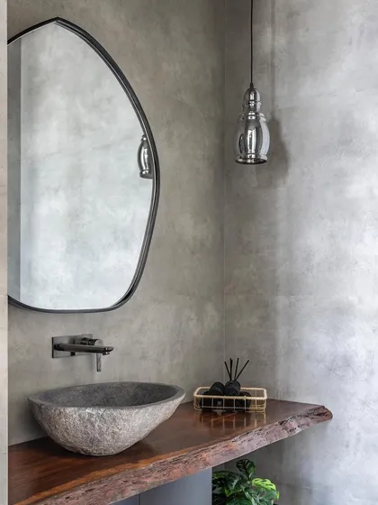 The powder bathroom combines the raw beauty of concrete walls with the organic warmth of a live-edge wood counter. A natural stone sink and a simple pendant light complete this study in texture and minimalism.