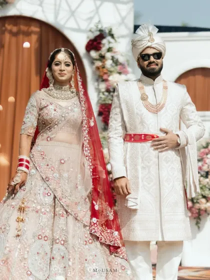 A modern couple's portrait. The bride's pastel lehenga with a red veil and the groom's white sherwani with a pop of red create a beautifully balanced and stylish color palette.