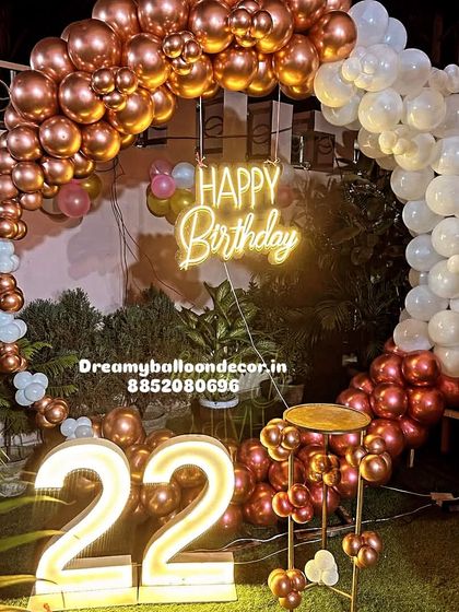 A stylish 22nd birthday party on a terrace at night. The balloon ring with a neon sign and light-up marquee numbers creates a fantastic party atmosphere under the open sky.