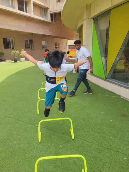 A young boy energetically jumps over hurdles during an outdoor fitness session. We use our green, open spaces to conduct dynamic drills that make exercise feel like play.